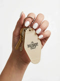 Cream retro keychain with 'The Dog Parent Club' logo, held in hand with white nails